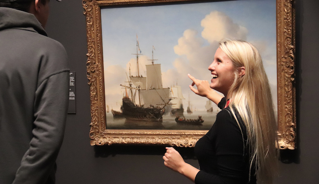 Woman pointing at a painting. A man looking at art.