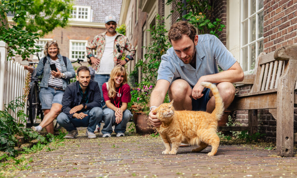 A man and a cat on a walk. People sitting on a bench in the background.