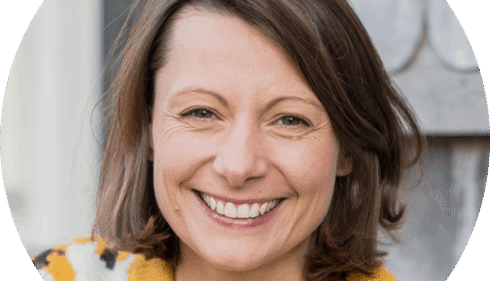 A smiling woman with brown hair and a yellow sweater.