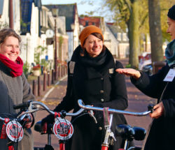 Tourist and guide talking while standing with bikes on Amsterdam street. Smiling women enjoying a bike tour.