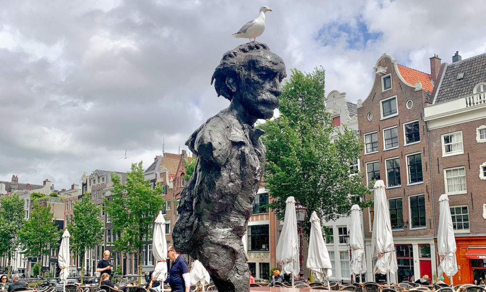 A statue of a boy with a bird on his head. The statue is in a public square.