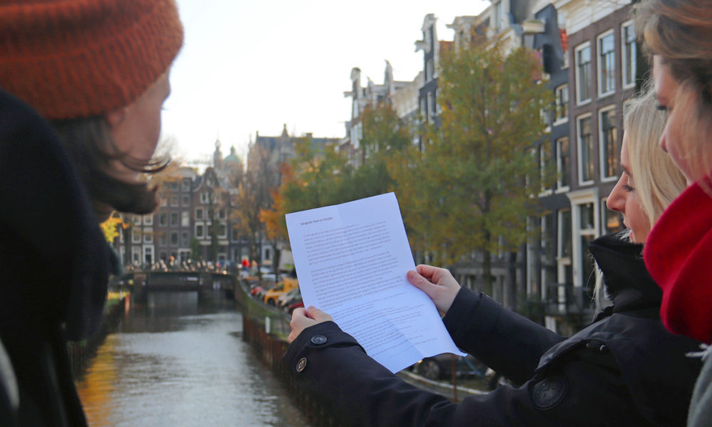 Two women looking at a map by a canal. They are planning their trip to Amsterdam.