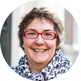 Portrait of a smiling woman with red glasses. She has short hair and a warm expression.