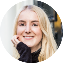 Blonde woman smiling and posing for a photo. She is wearing a black sweater.