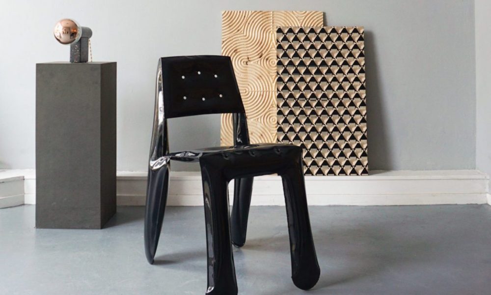 A sleek black chair sits in front of modern art pieces. The chair features a simple design with holes in the backrest.