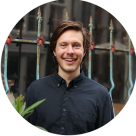 A smiling man in a black shirt standing in Amsterdam.