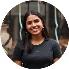 A young woman with long dark hair and gold hoop earrings. She is smiling and wearing a black t-shirt.