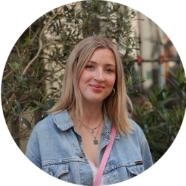 A young woman with blonde hair smiling. She is wearing a denim jacket.